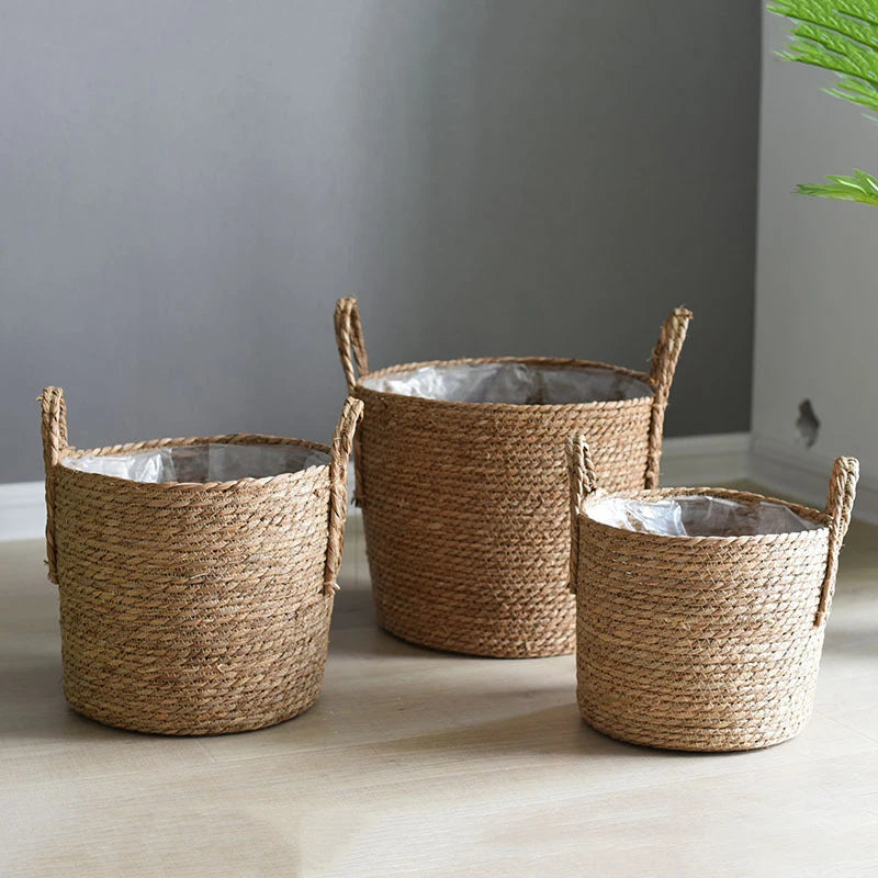 Three woven baskets with handles on a light wooden floor against a gray wall.