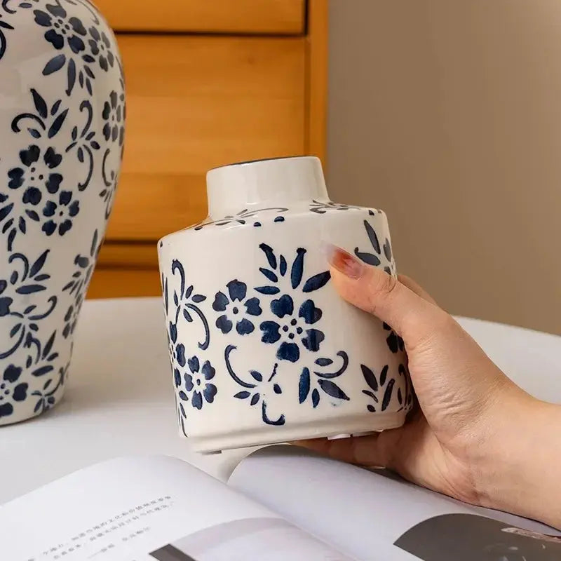 Hand holding a white ceramic vase with blue floral patterns