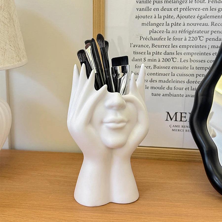 White face-shaped holder with makeup brushes on a wooden surface