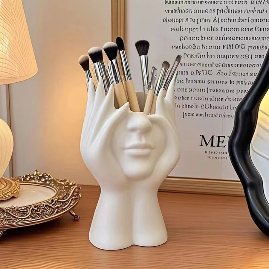 White ceramic hand-shaped brush holder with makeup brushes on a wooden surface.