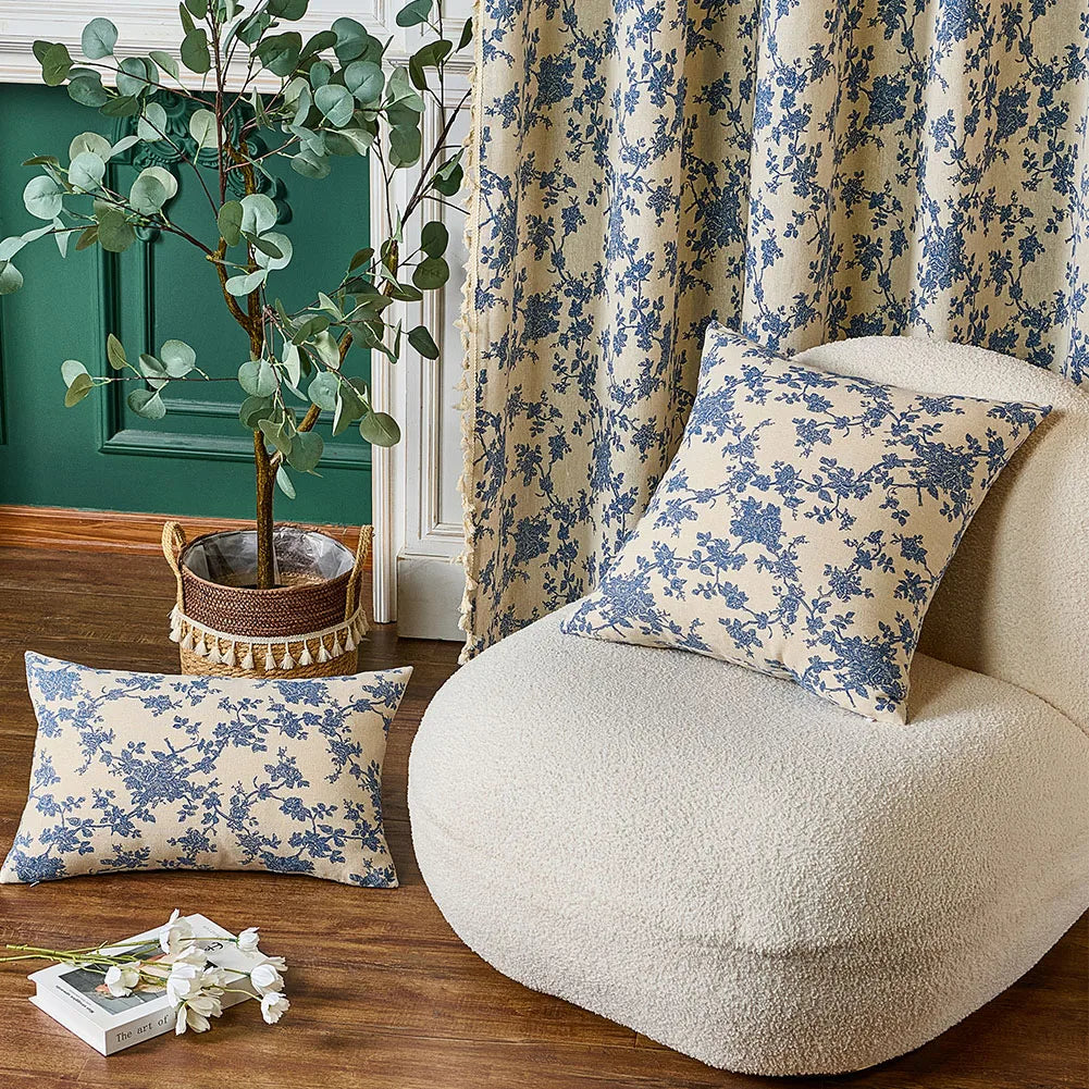 Floral-patterned cushions on a textured chair with a plant and decor items in the background.