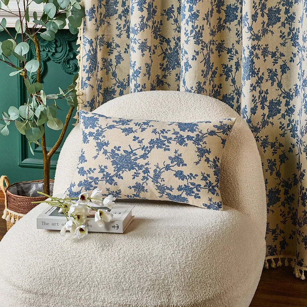 Decorative pillow with blue floral pattern on a white chair against a floral curtain.
