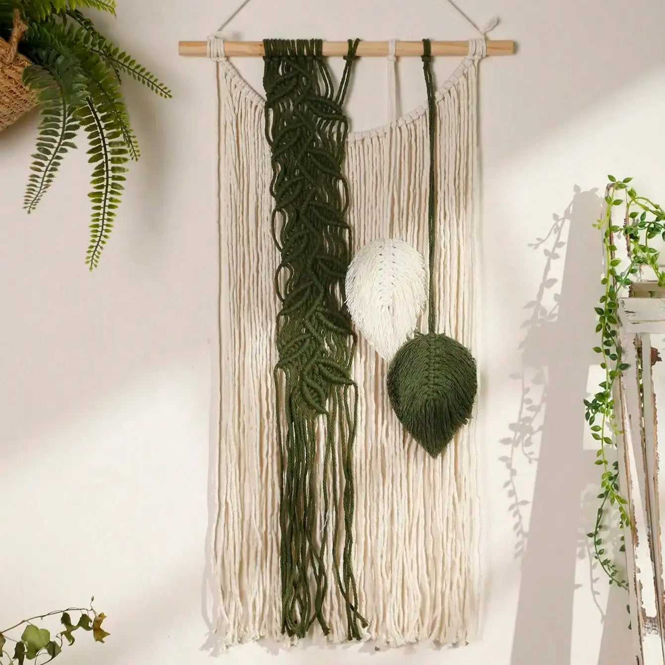 Macrame wall hanging with green and beige elements on wall.