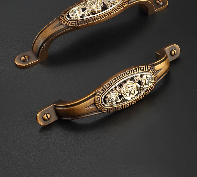 Two ornate bronze handles with floral designs on a dark background