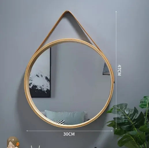 Round wooden mirror with a strap on a gray wall, with measurements indicated.
