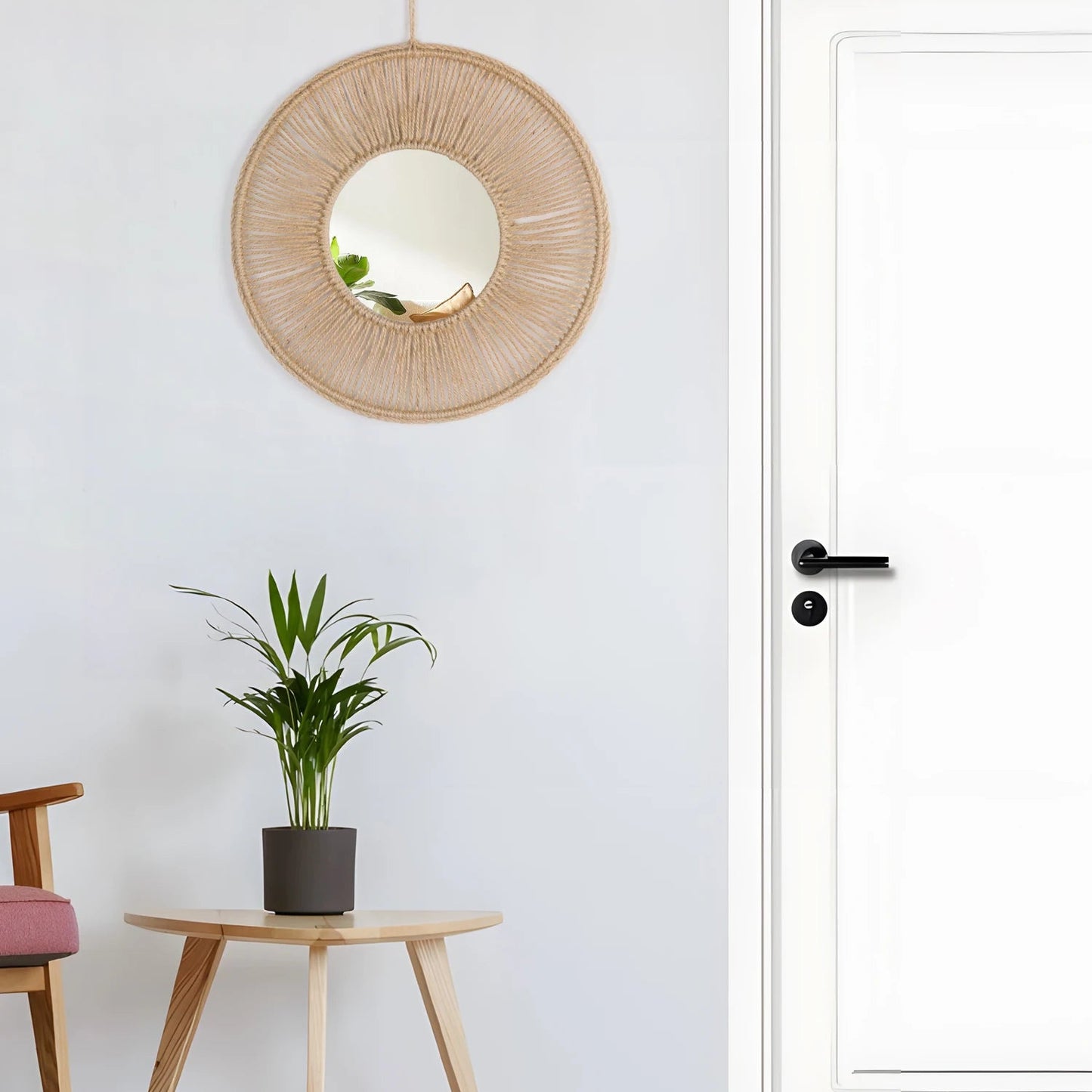 Woven round mirror on a white wall with a plant and chair in the foreground.