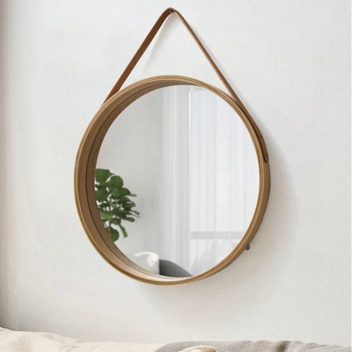 Round mirror with wooden frame on a white wall, with a cat-shaped pillow on a sofa below.