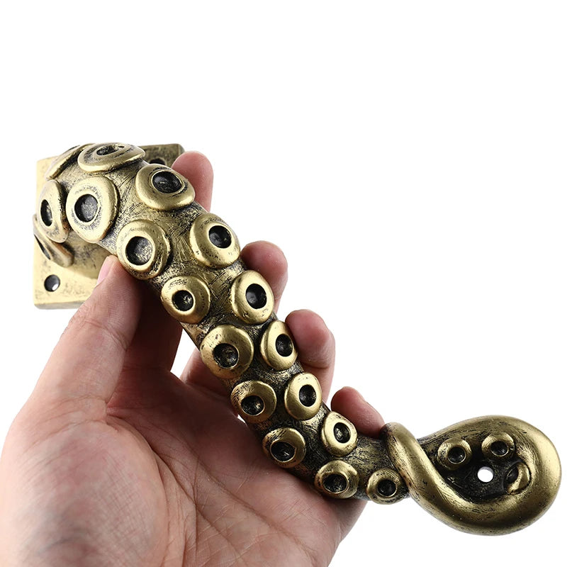 Brass octopus handle held in a hand against a white background