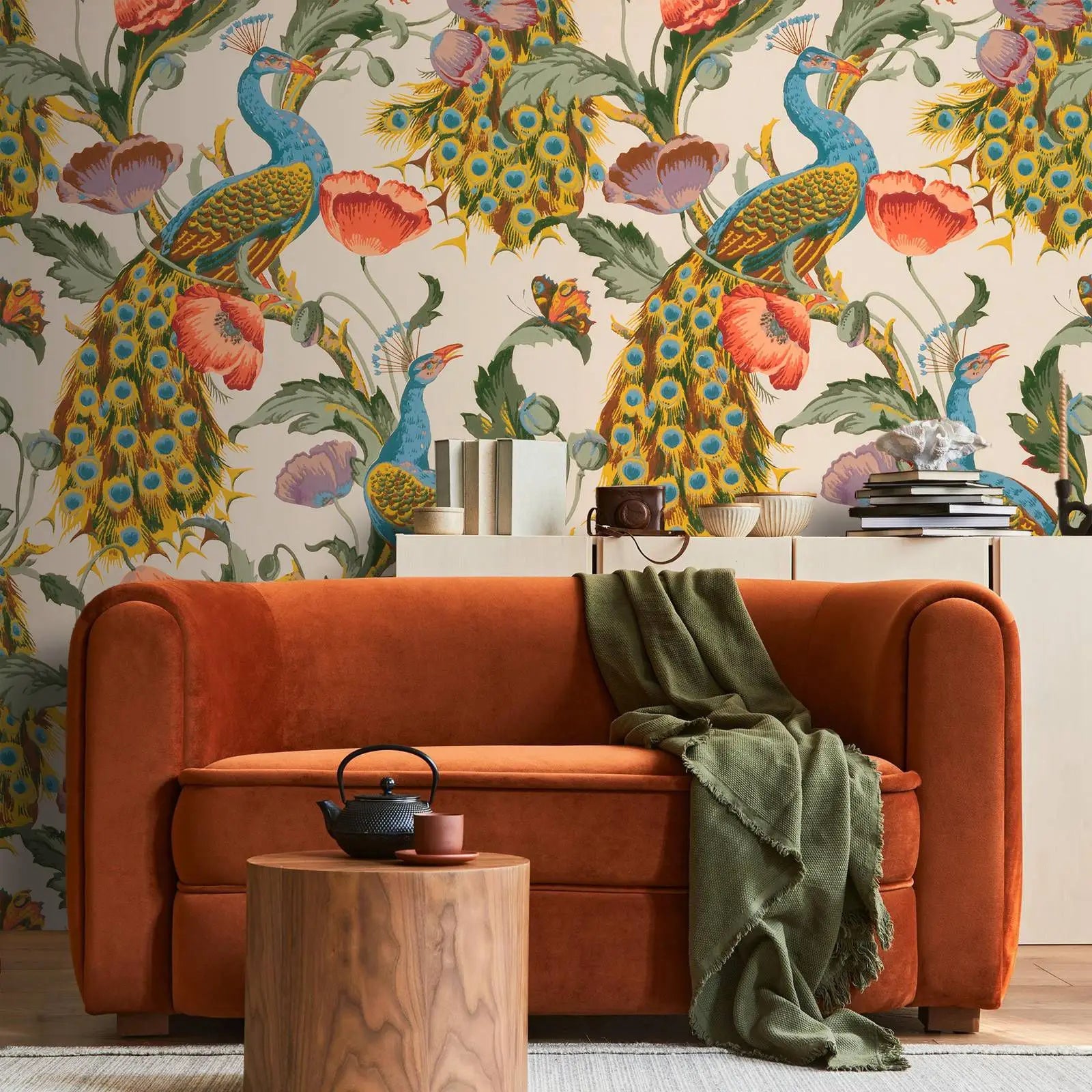 Orange sofa with a green blanket in front of peacock and floral wallpaper