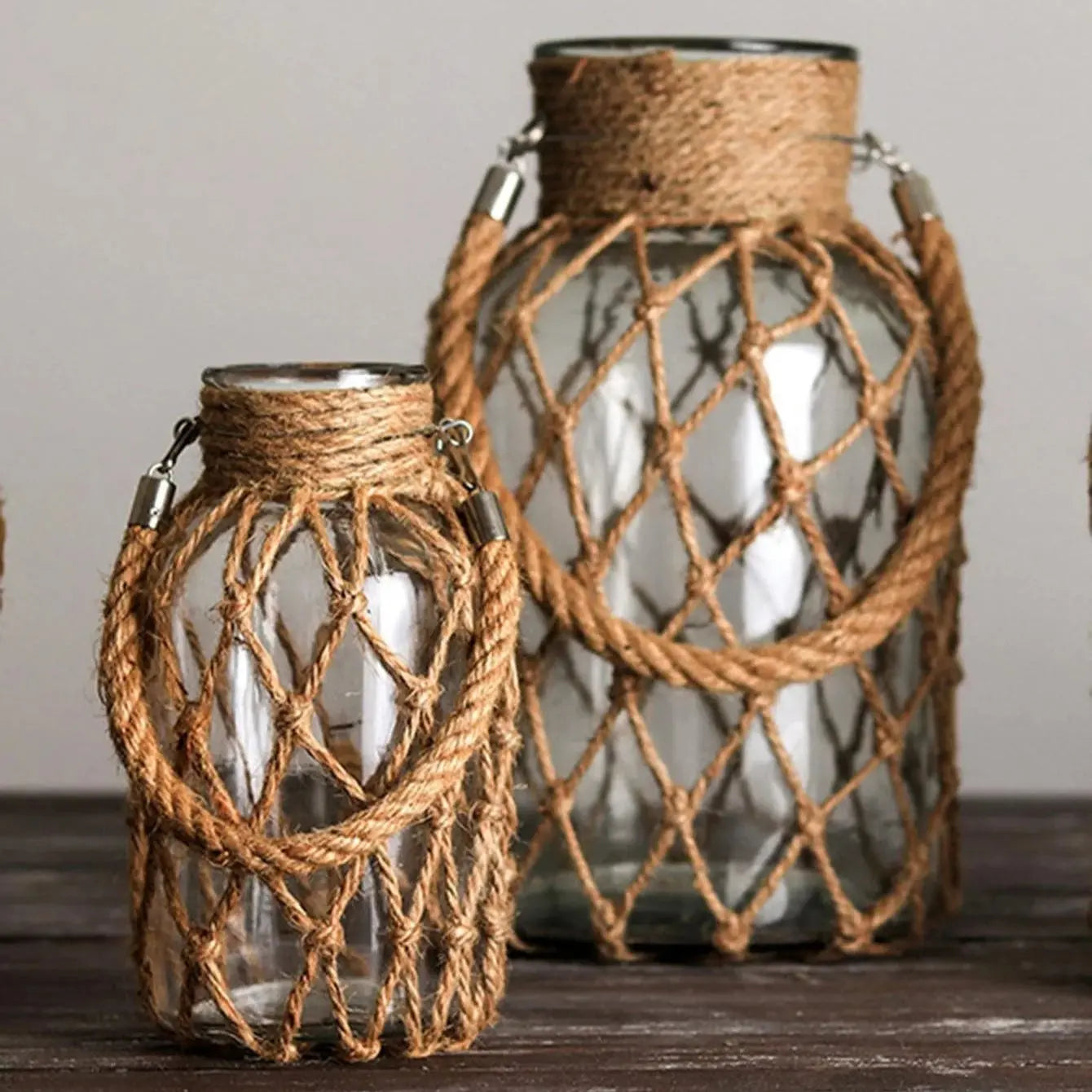 Two glass lanterns with rope netting on a wooden surface