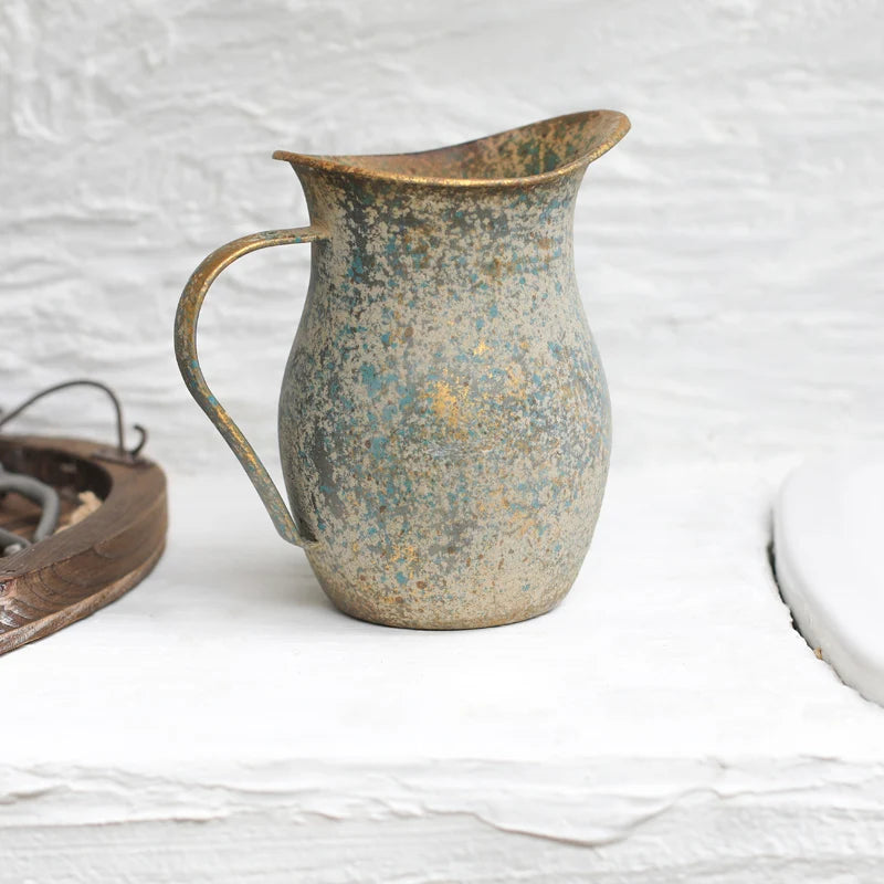 Rustic metal pitcher on a textured white surface