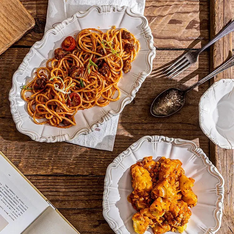Two plates of pasta on a wooden table with a cookbook open.