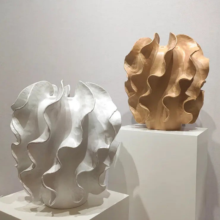 Two abstract sculptures, one white and one gold, on a white platform with a plain background.