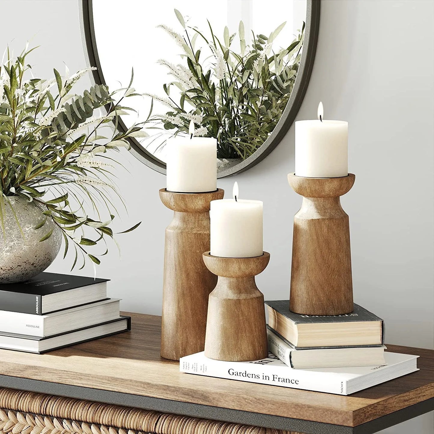 Decorative setup with candles in wooden holders, books, and plants on a shelf.