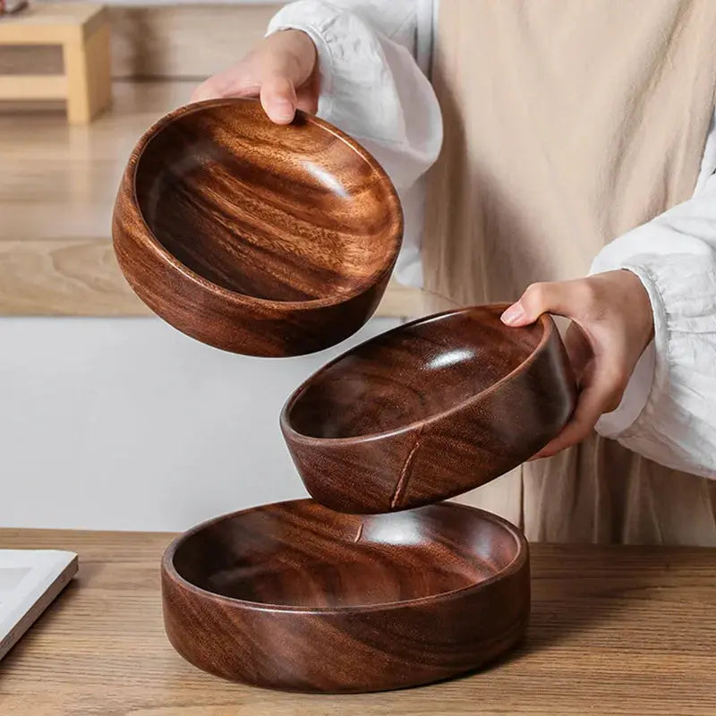 Person holding a stack of wooden bowls on a wooden surface
