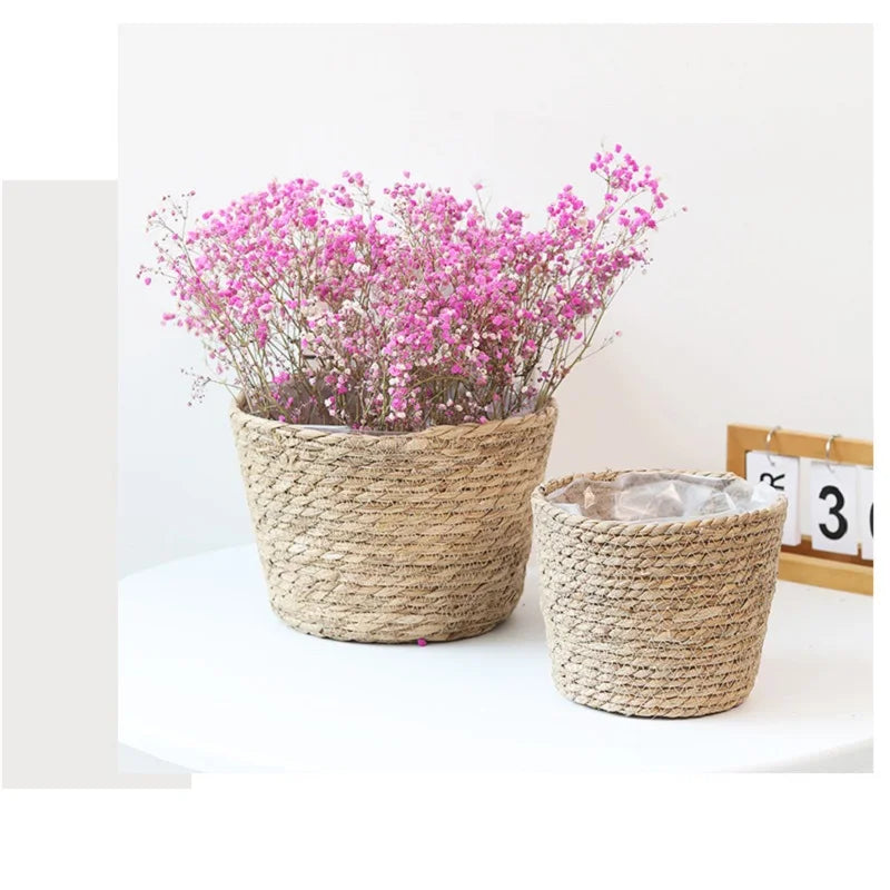 Two woven planters with pink flowers and a clear container on a white surface.