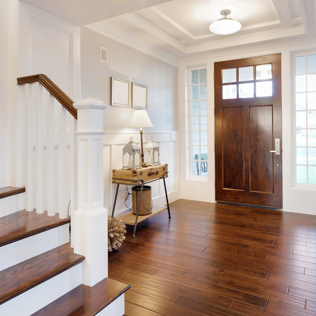 Foyer with wooden staircase, door, and side table with lamp.