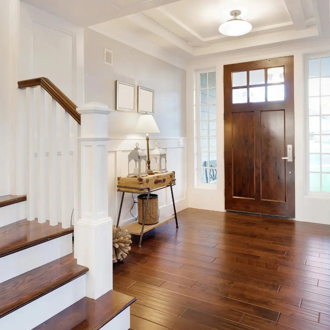 Foyer with wooden staircase, door, and side table with lamp.
