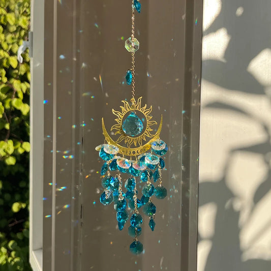 Decorative sun and moon hanging ornament with blue crystals on a glass surface.
