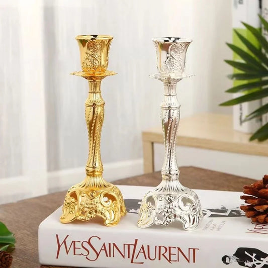 Gold and silver candlesticks on a Yves Saint Laurent book with a plant in the background