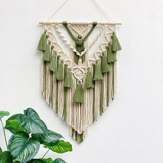 Macrame wall hanging with green and beige colors on a white wall.