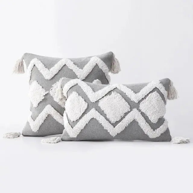 Two gray pillows with white geometric patterns and tassels on a light gray background
