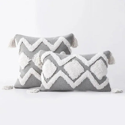 Two gray pillows with white geometric patterns and tassels on a light gray background