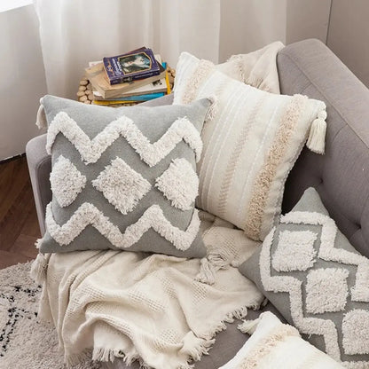 Gray and white textured pillows on a sofa with a blanket and books.
