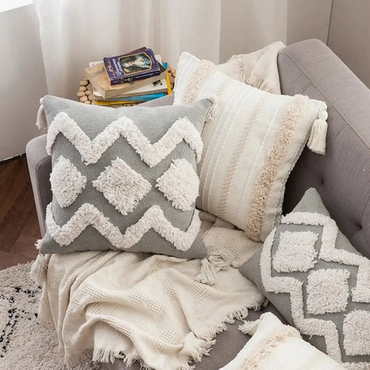 Gray and white textured pillows on a sofa with a blanket and books.
