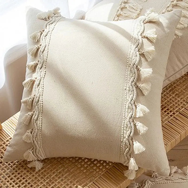 Beige pillow with tassel trim on a wicker surface