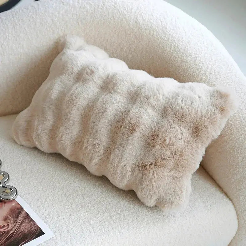 Beige fluffy pillow on a white surface with a blurred photo in the corner.