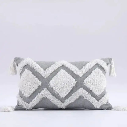 Gray and white pillow with geometric pattern and tassels on a light gray background