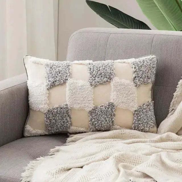 Decorative pillow with a checkered pattern on a gray sofa with a blanket.