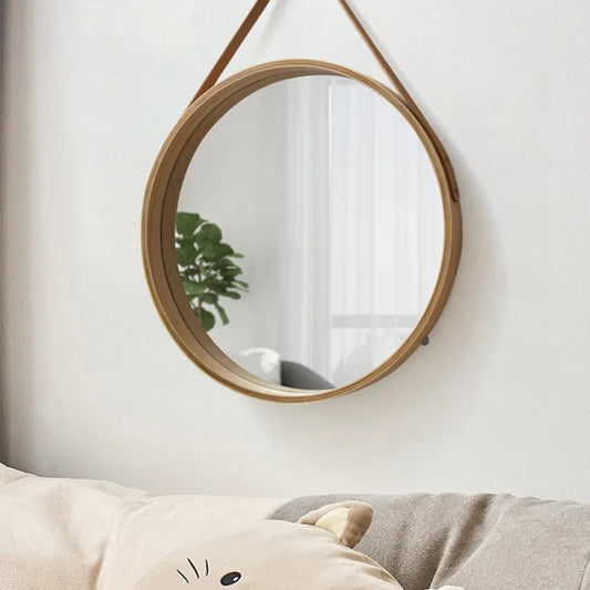 Round wooden-framed mirror on a white wall with a plant reflection