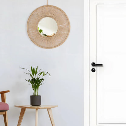 Woven round mirror on a white wall with a plant and chair in the foreground.