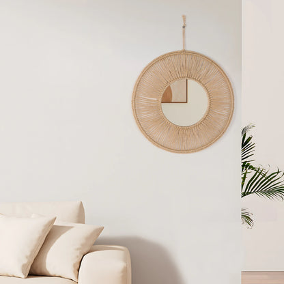 Round woven mirror on a wall above a beige sofa with a plant in the corner.