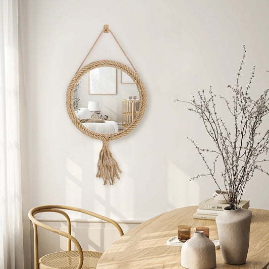 Round woven mirror with tassels hanging on a wall above a table with decor items.