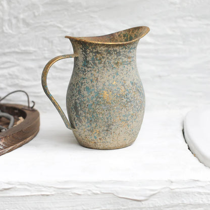 Rustic metal pitcher on a textured white surface