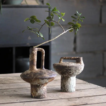 Two rustic ceramic vases with handles on a wooden surface