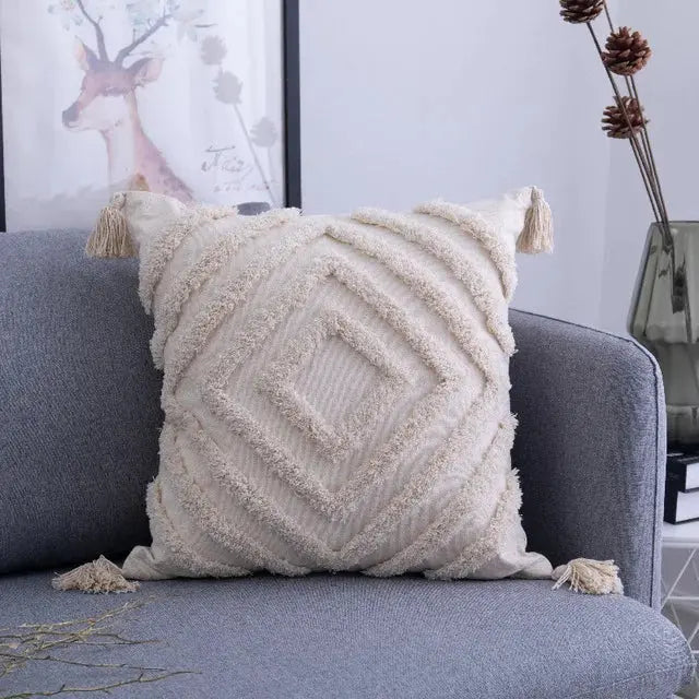 Textured beige pillow with tassels on a gray sofa in a living room setting.