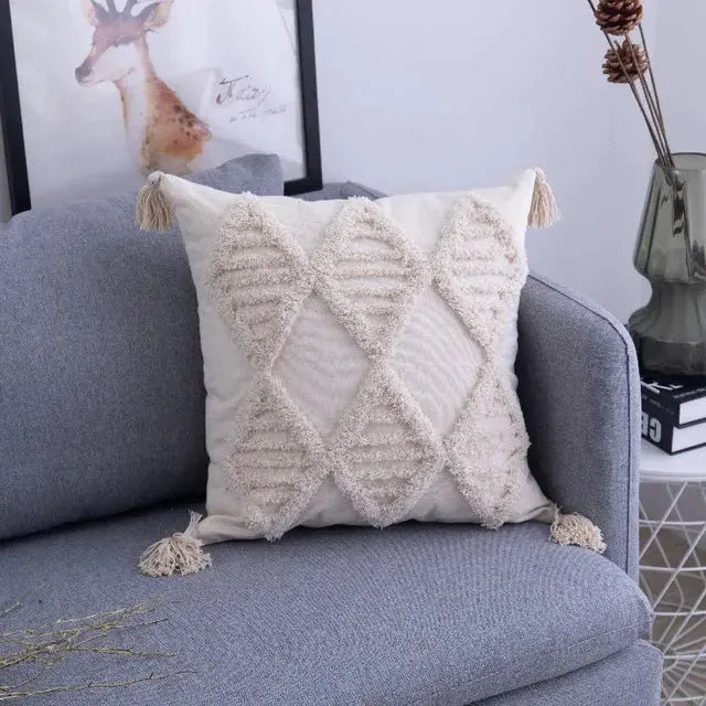 Decorative pillow with tassels on a gray sofa, with a framed picture of a deer in the background.