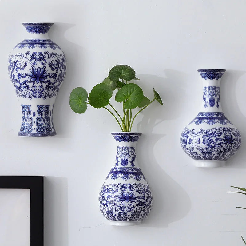 Three blue and white patterned vases on a white wall with a plant in one of them.