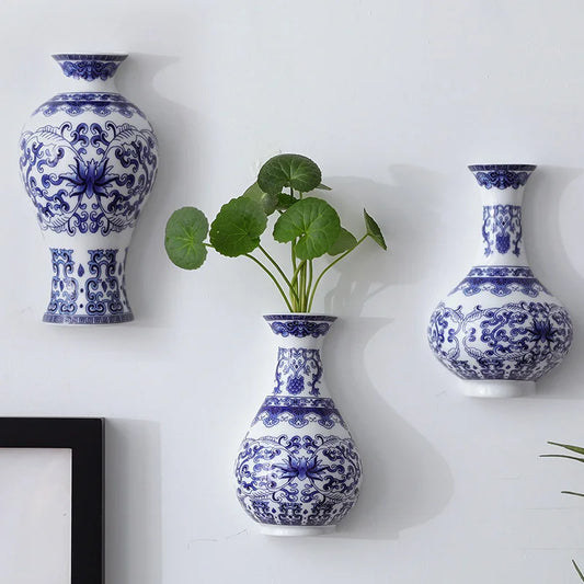 Three blue and white patterned vases on a white wall with a plant in one of them.