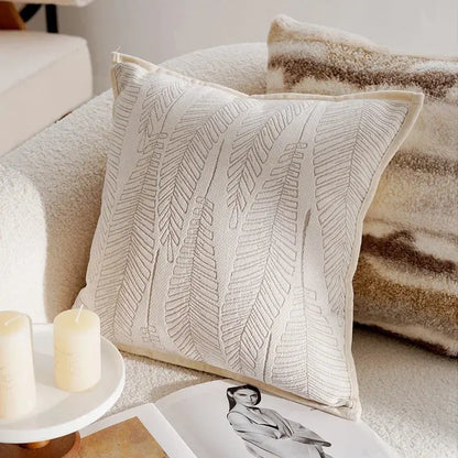 Decorative pillow with leaf pattern on a couch with candles and a magazine.